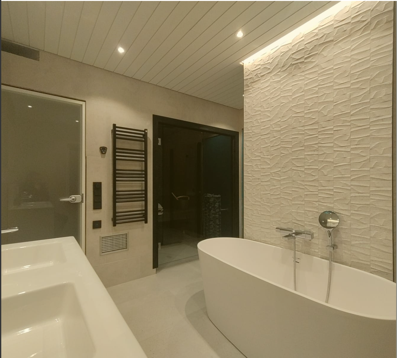 Moderni kylpyhuone valkoisella ammeella, strukturoidulla valkoisella laattaseinällä ja lasisuihkulla